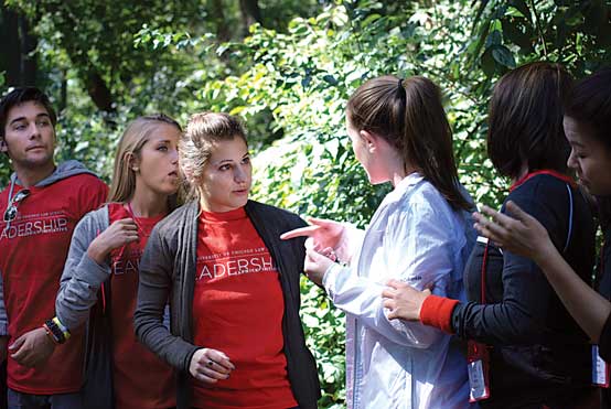 A cohort negotiates an exercise where students rearrange themselves in height order on a beam without falling off