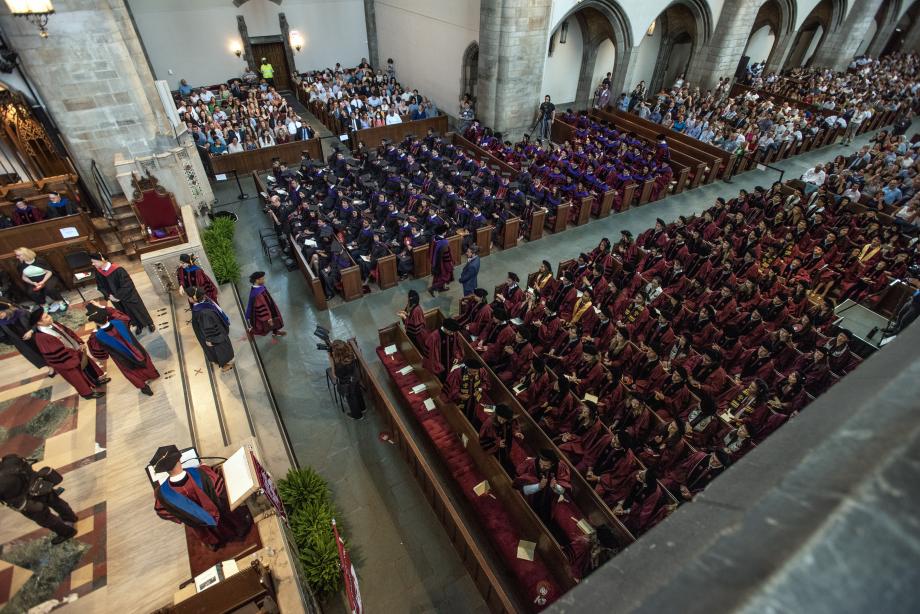 View from balcony in Rockefeller Chapel showing a speaker at the podium and the graduates seated in pews and receiving their diplomas on stage.