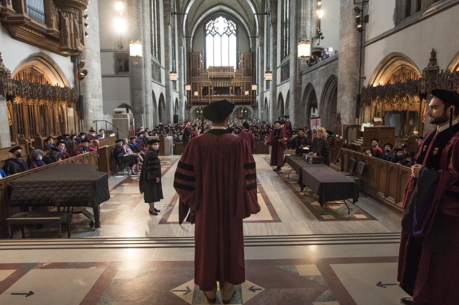 The back of a student about to head forward to receive a diploma. A wide shot of the chapel is shown.