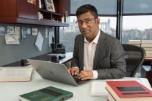 Aziz Huq sitting in his office with his laptop in front of him.