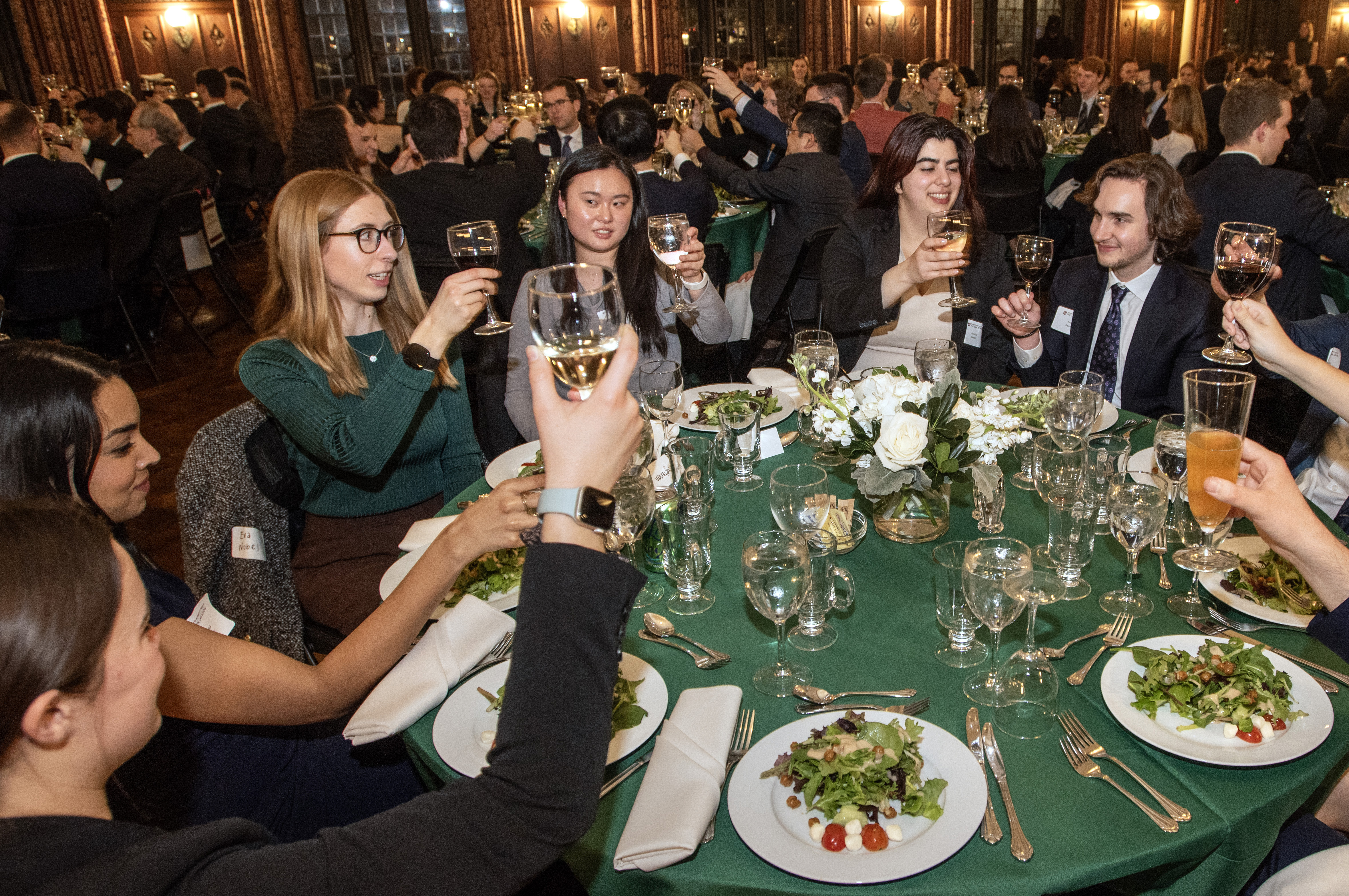 Students seated around a table raise their glasses to cheers.