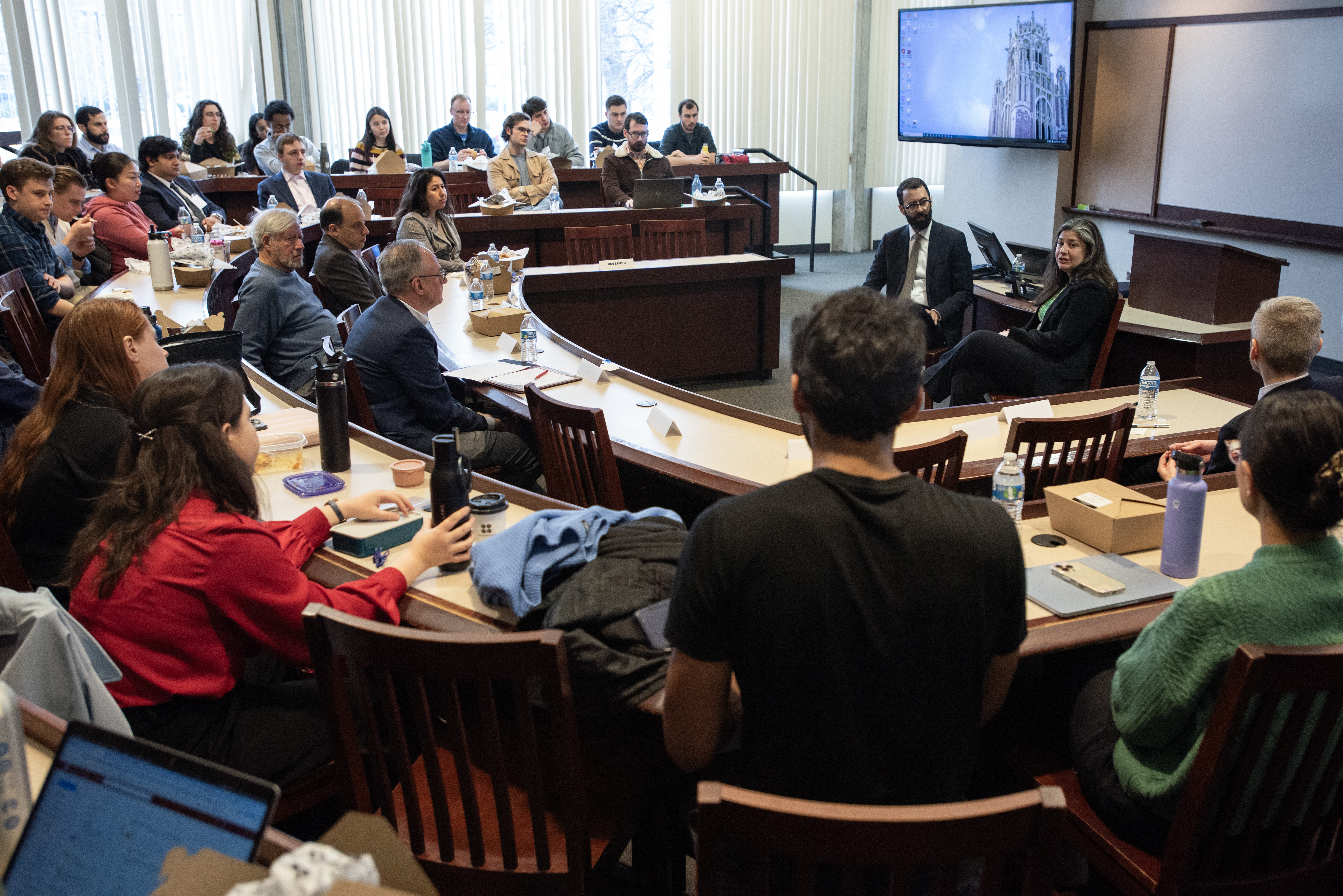 A classroom filled with students listening to Judge Bloomekatz, who is sitting and speaking at the front of the room, sitting next to Professor John Rappoport.