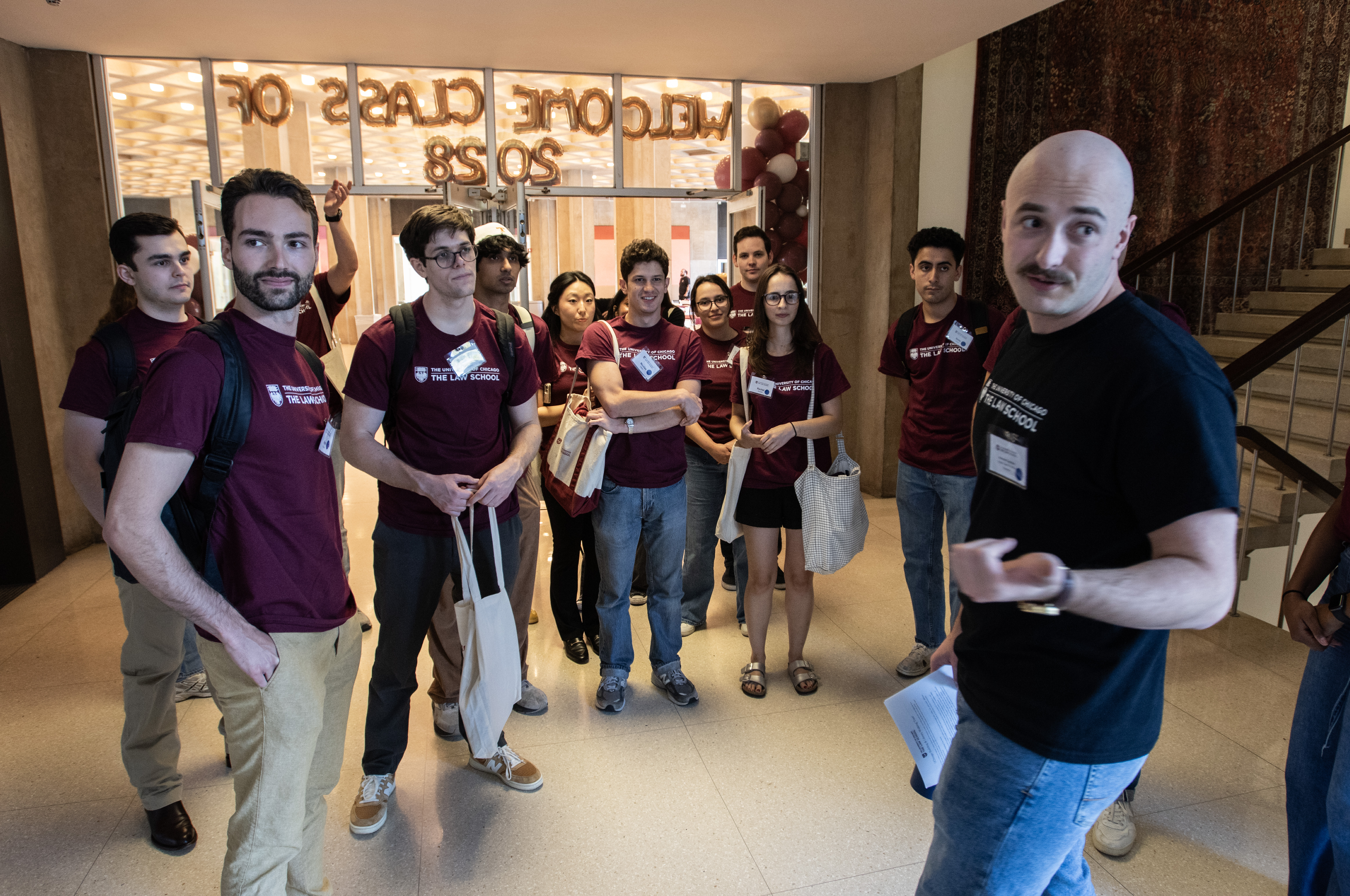 A male student wearing a black shirt guides students who are wearing maroon shirts down a hallway.