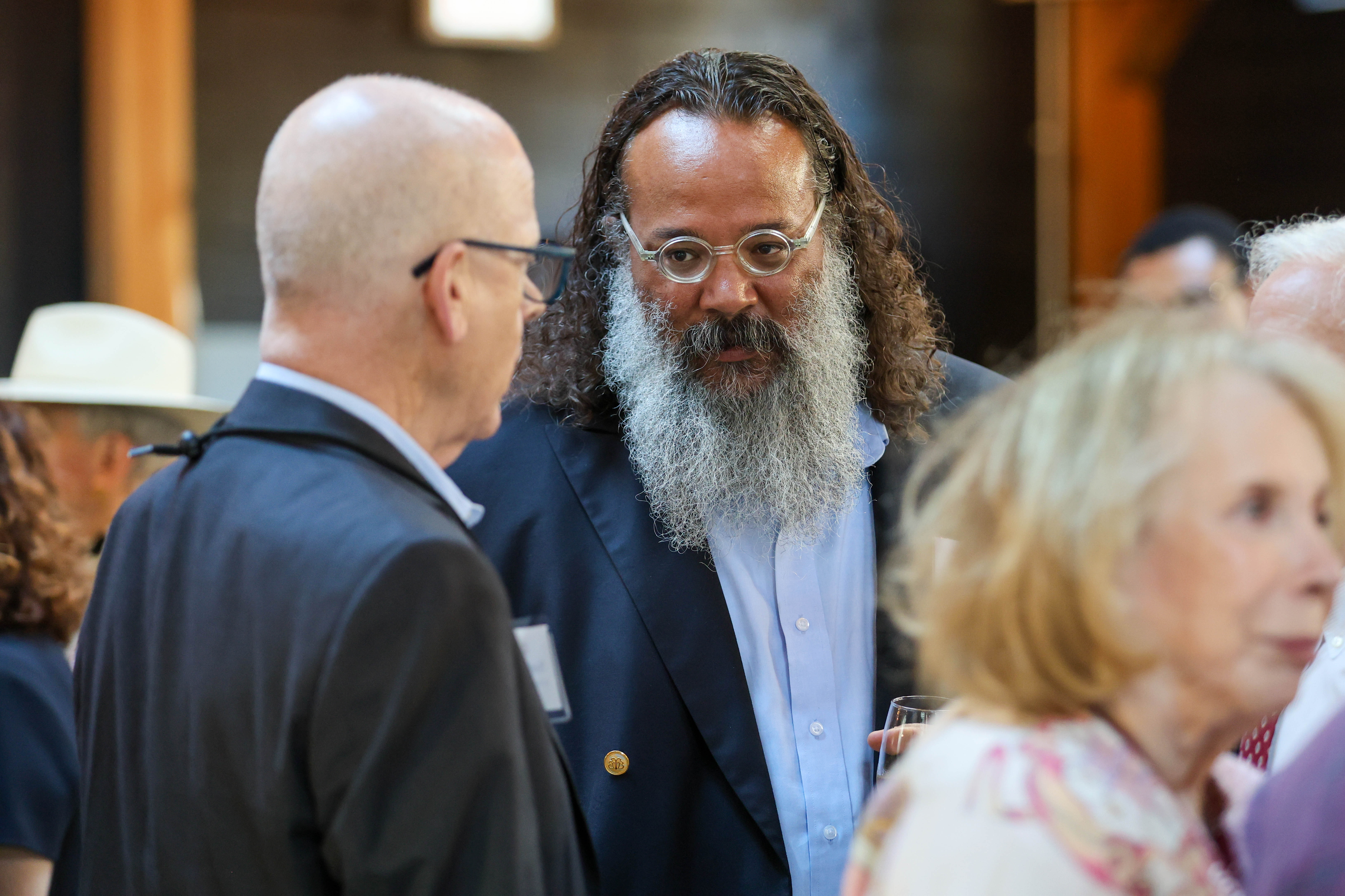 A man with a long beard speaks to a man with a bald head.