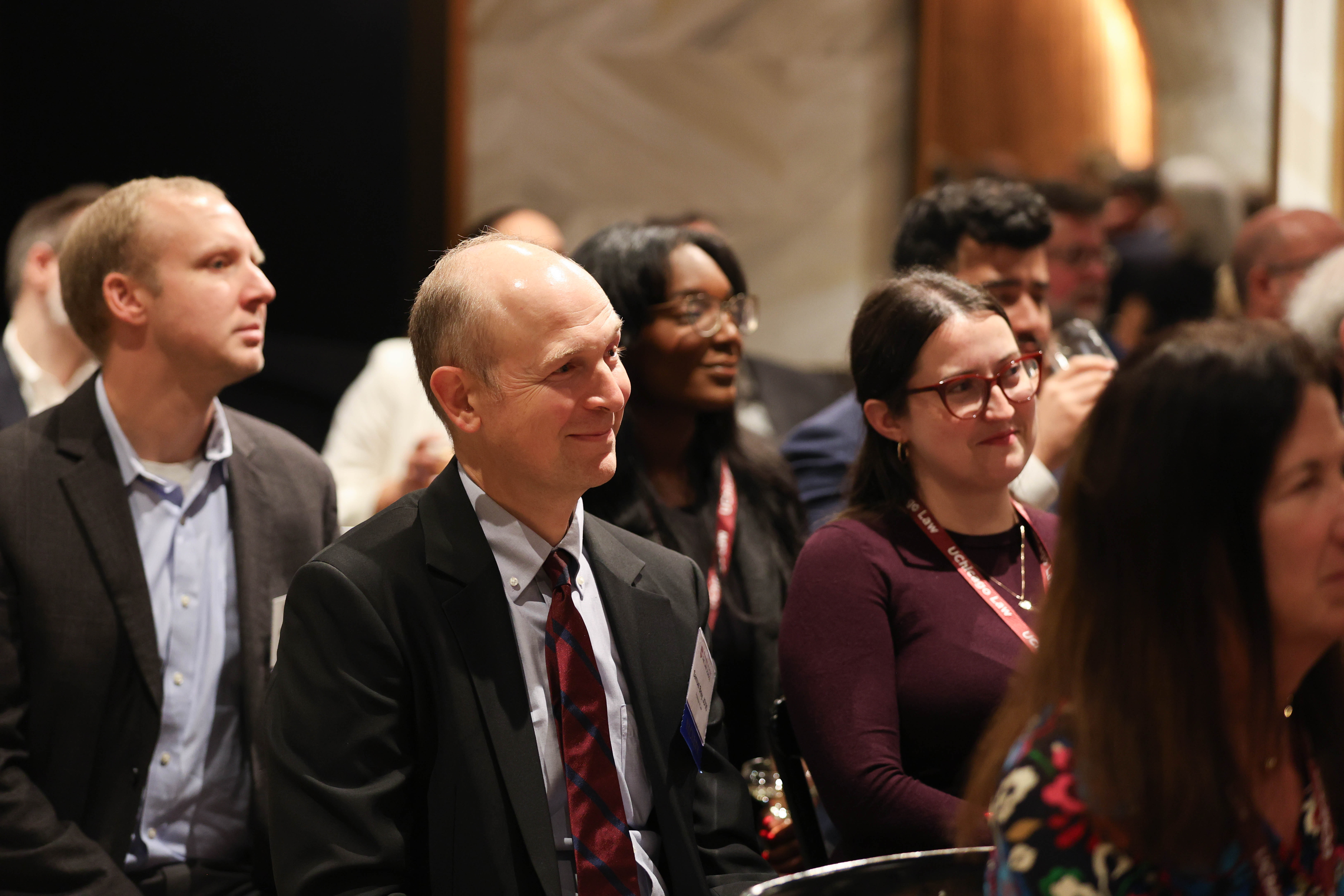 A view of people seated in rows while looking ahead to a person delivering a speech.