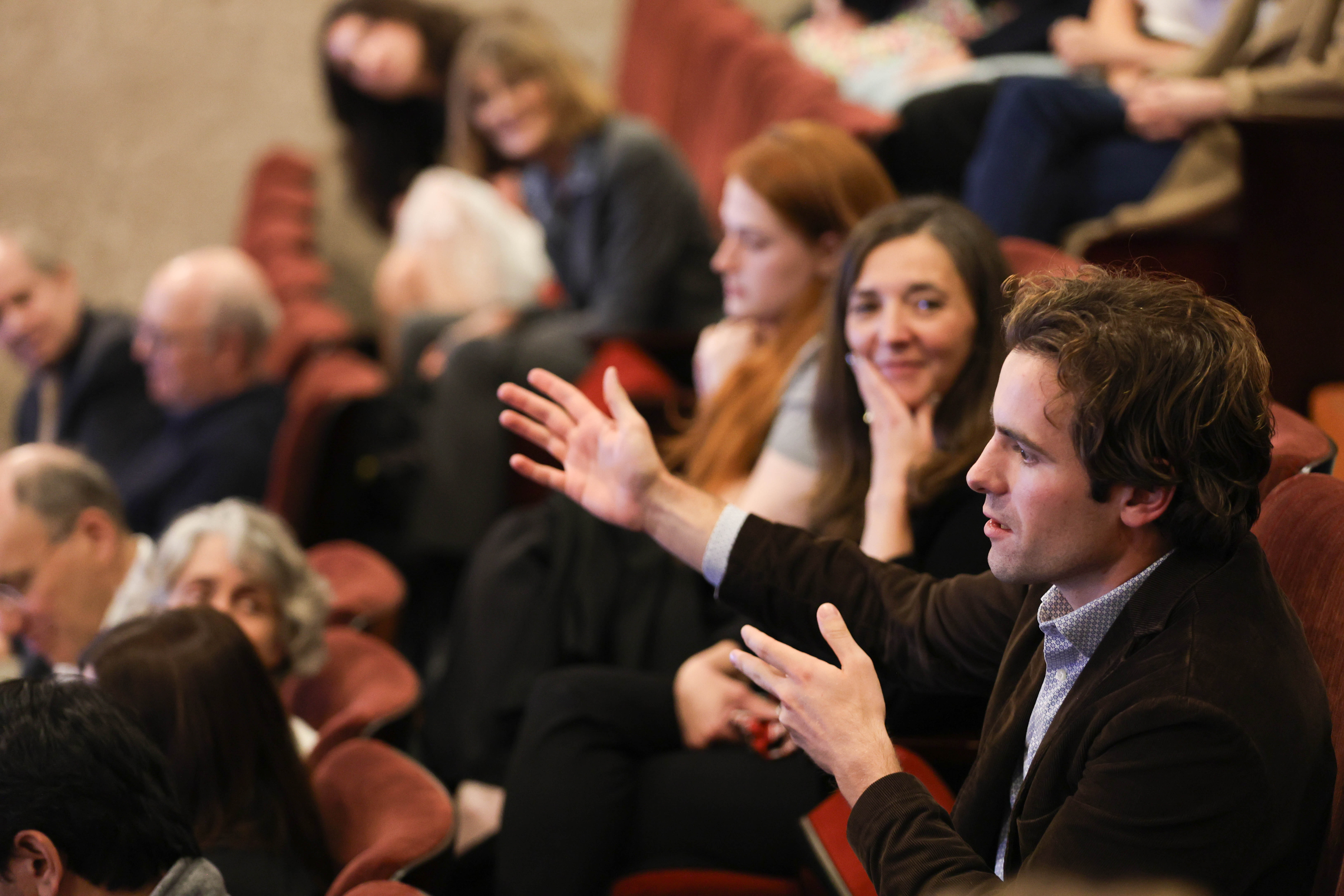 A view of the seated audience with one man appearing to ask a question.