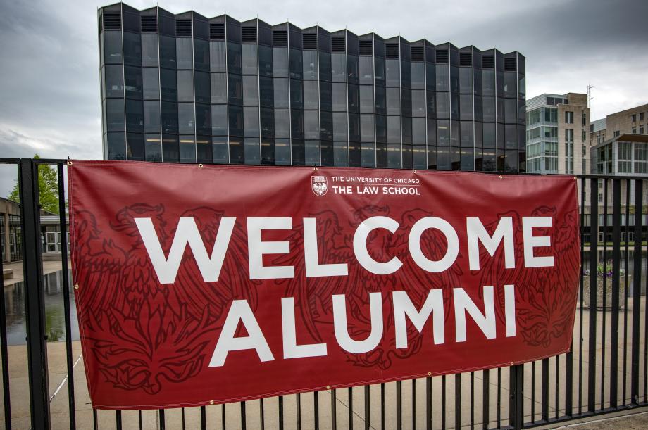 A banner proclaiming, "Welcome Alumni" hangs on a fence in front of the Law School building.