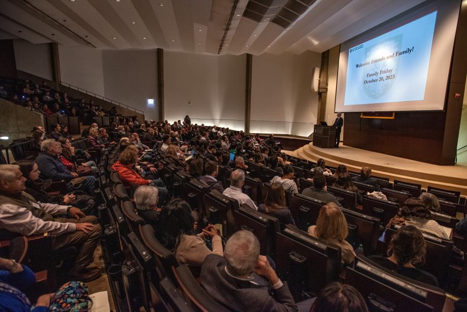 An auditorium full of people with a slideshow. The slide says "Welcome Friends and Family! Family Friday. October 20, 2023."