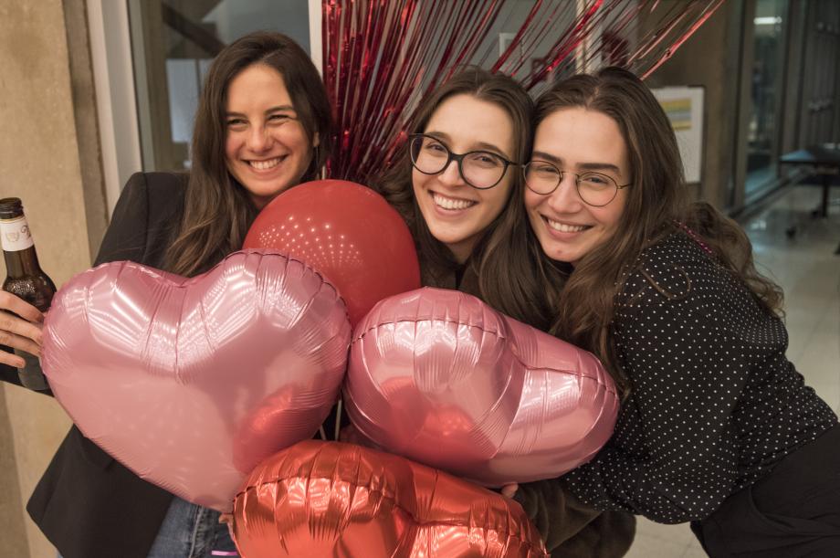 Three women pose with red and pink balloons.