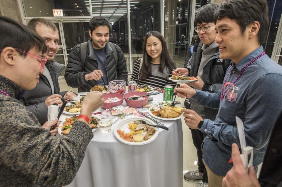 Six students with plates of food circle around a hightop table.