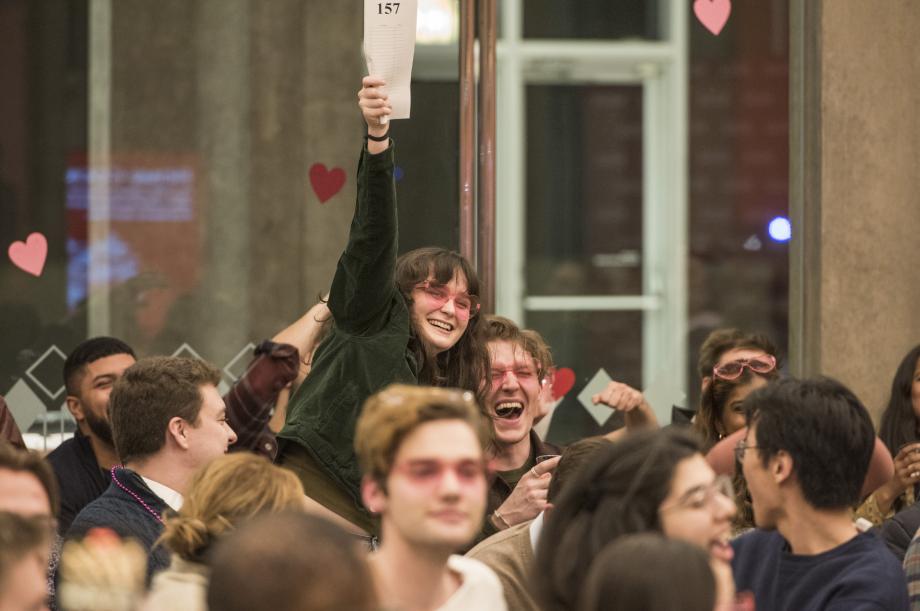 With pink heart glasses, Brynne Follman jumps out of her seat clutching her bid card raised high.