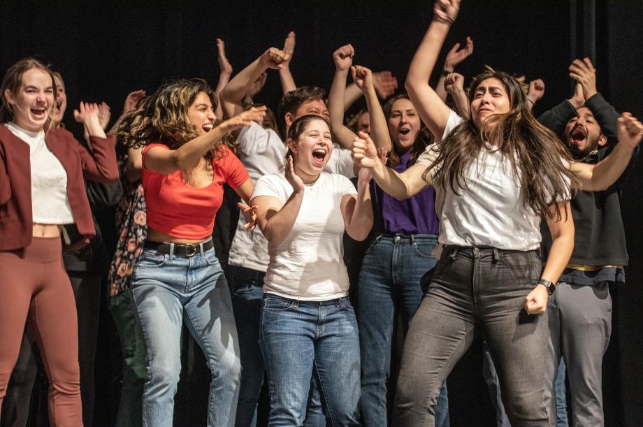 Students with their right hands raised up, looking very cheerful. 