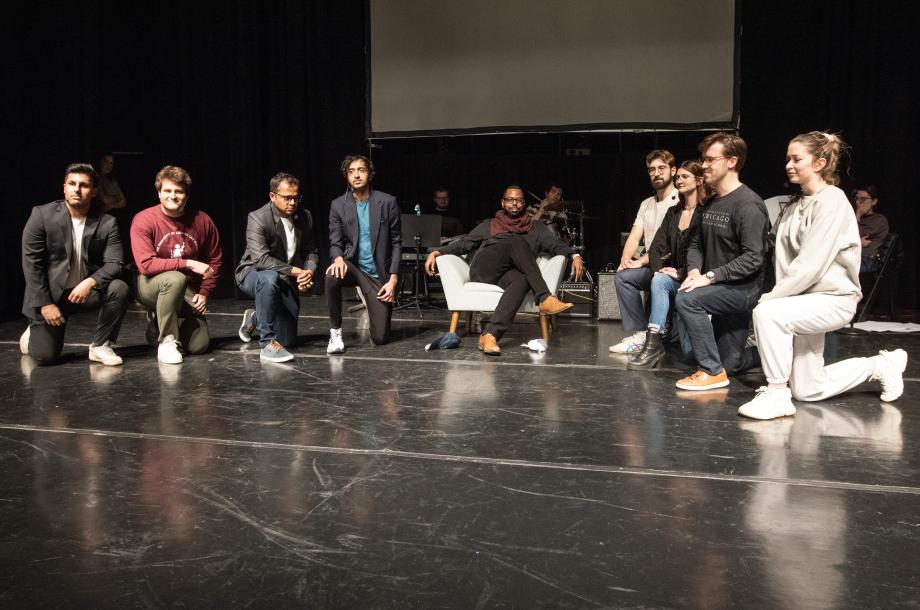 8 people with one leg on the ground as someone lounges on a white, comfortable chair.