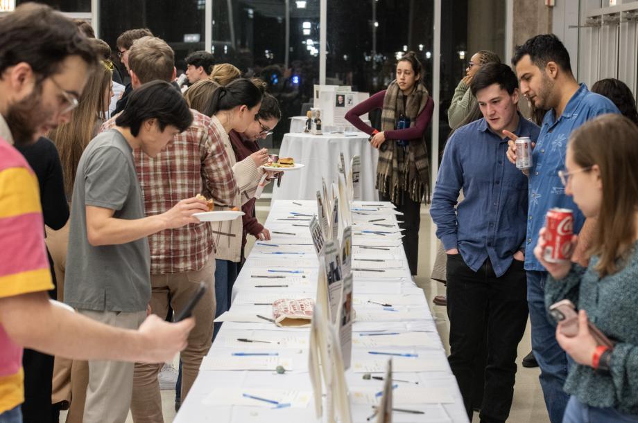 A table with papers and pens. Two rows of students walking down the tables and looking at the papers.