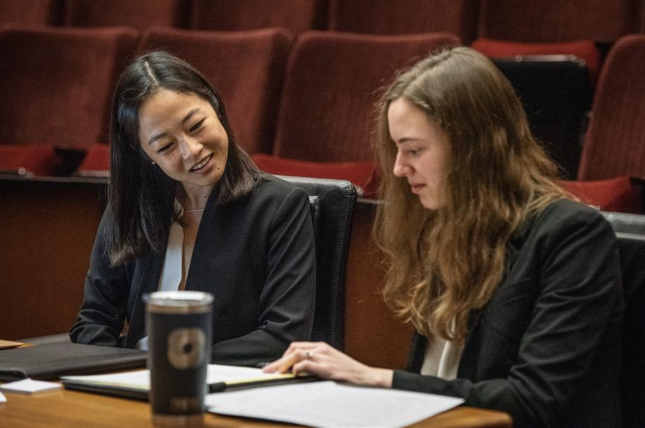 Two students in professional attire look at a legal pad in a folio.