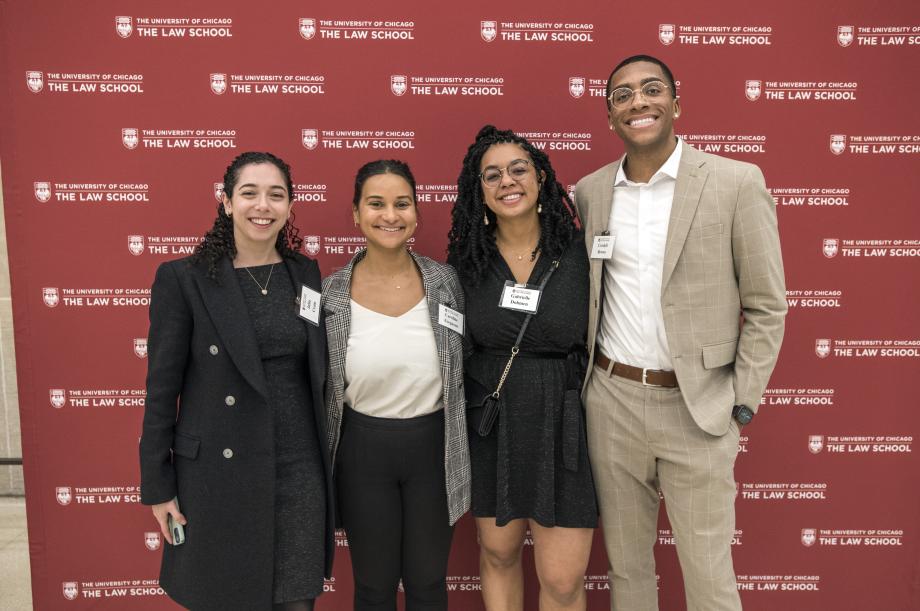Four students pose for the camera in front of a banner with the Law School logo