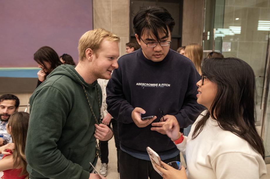 Three students chatting, with their phones in hand.