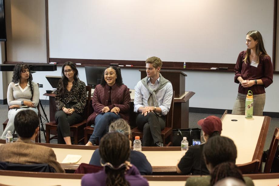 4 people sitting down and 1 person standing up in front of a class