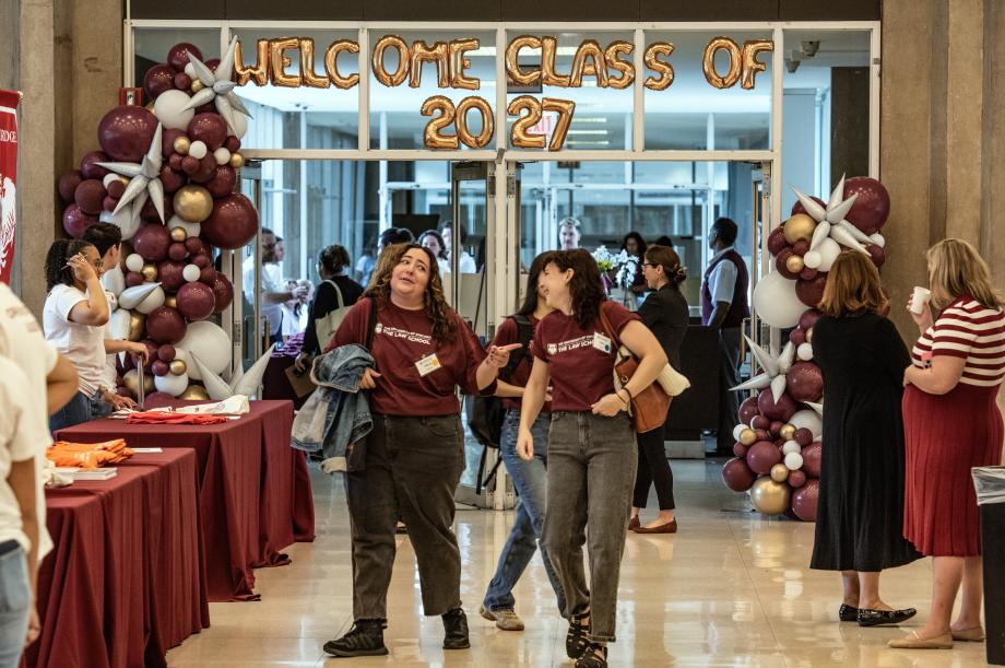 Two new students in matching maroon shirts smile at each other. Above them balloons spell out, “Welcome Class of 2027.”