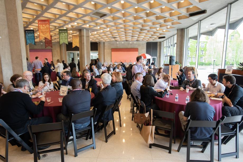 Dozens of alumni seat at round tables with class years displayed on the tables.