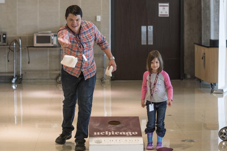 An alumnus throws bean bags with his young daughter