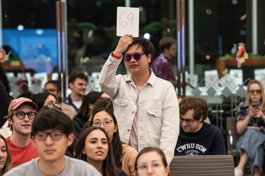Student in crowd standing up and raising a "69" paddle.