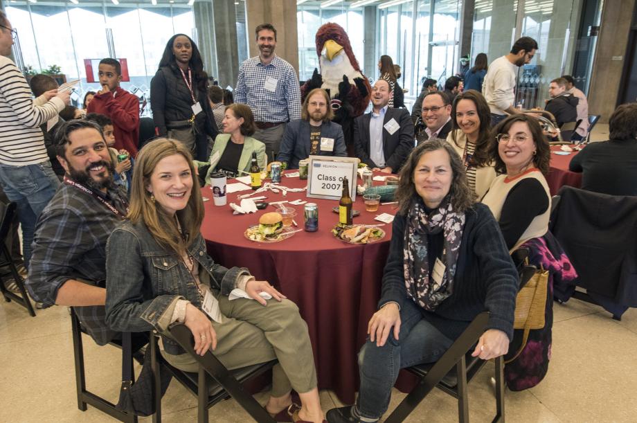 Several alumni and family members sit around a table with the Phil the Phoenix mascot