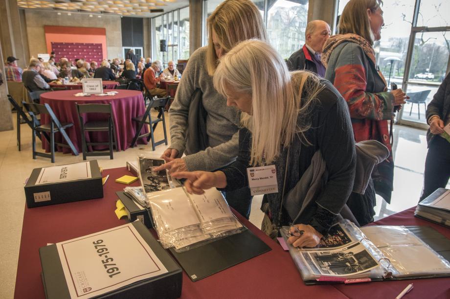 Two alumni look through binders of photographs