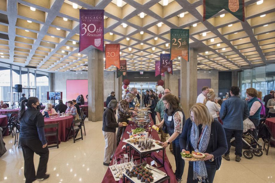 Alumni and family members line up along a long banquet table of buffet food