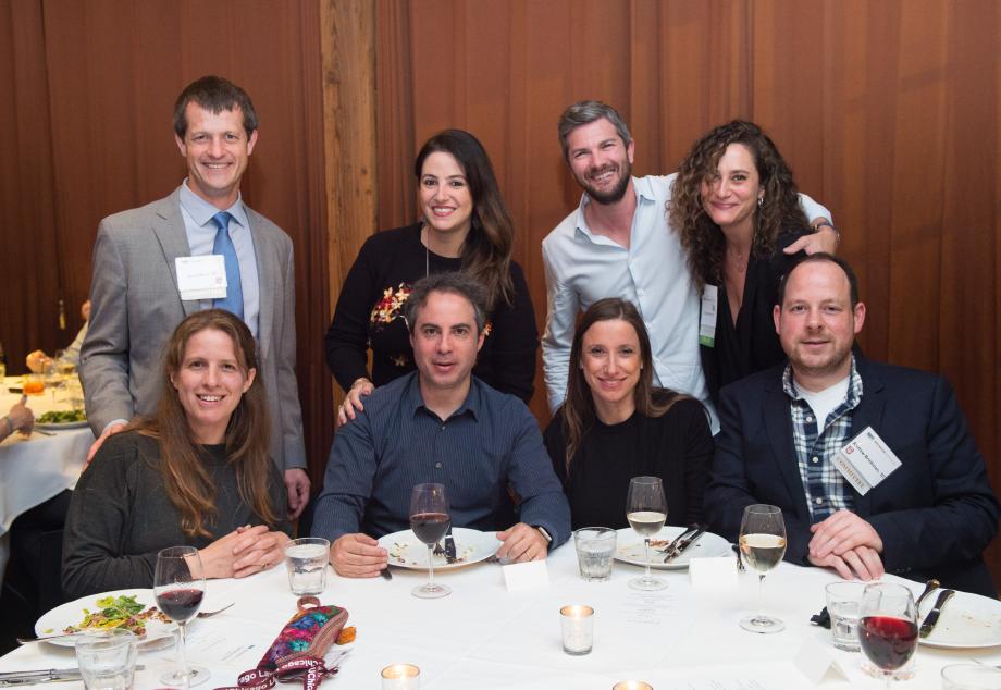 Seven alumni and family members pose for a group photo at a dinner table