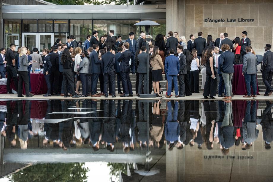 New students in professional attire mill about outside. Their reflects are caught in the Reflecting Pool.