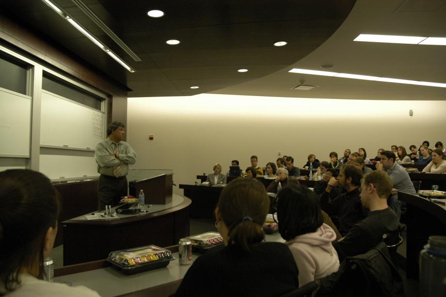 Stone stands in the front of a classroom with students filling the seats in front of him.