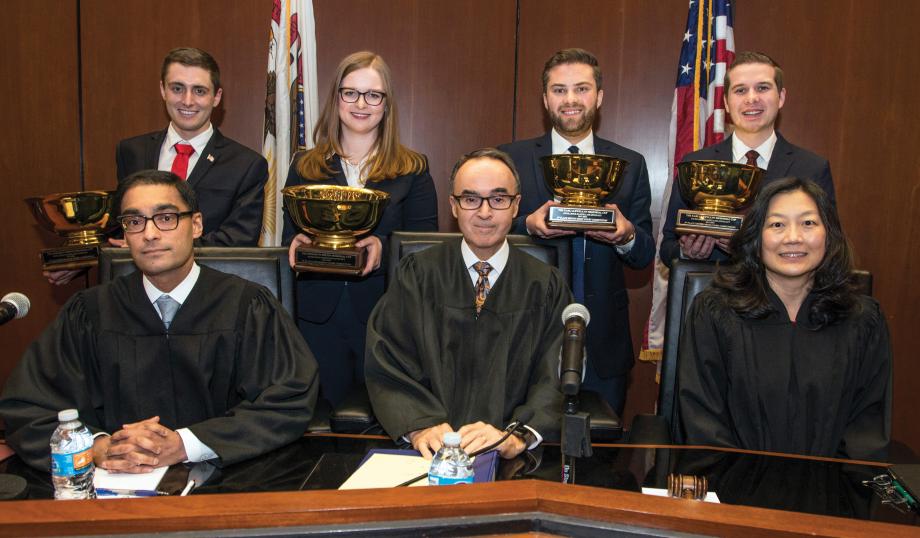 First- and second-place winners hold their trophies while standing behind robed judges