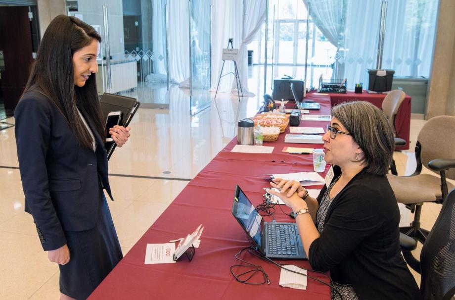 Lois sitting at a desk and speaking with a student dressed for an interview