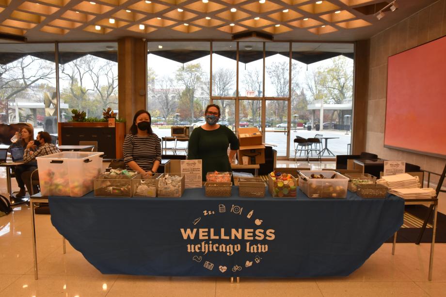 Two staff members behind a wellness table covered with plastics bins filled with items for assembling DIY stress kits.