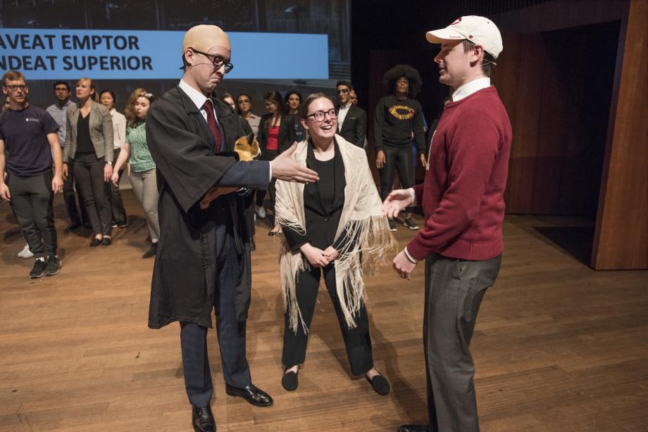 The characters of Judge Pawsner, Charlene Pawsner, and Eric Pawsner (wearing a red sweater with an H on the front). talk on stage.