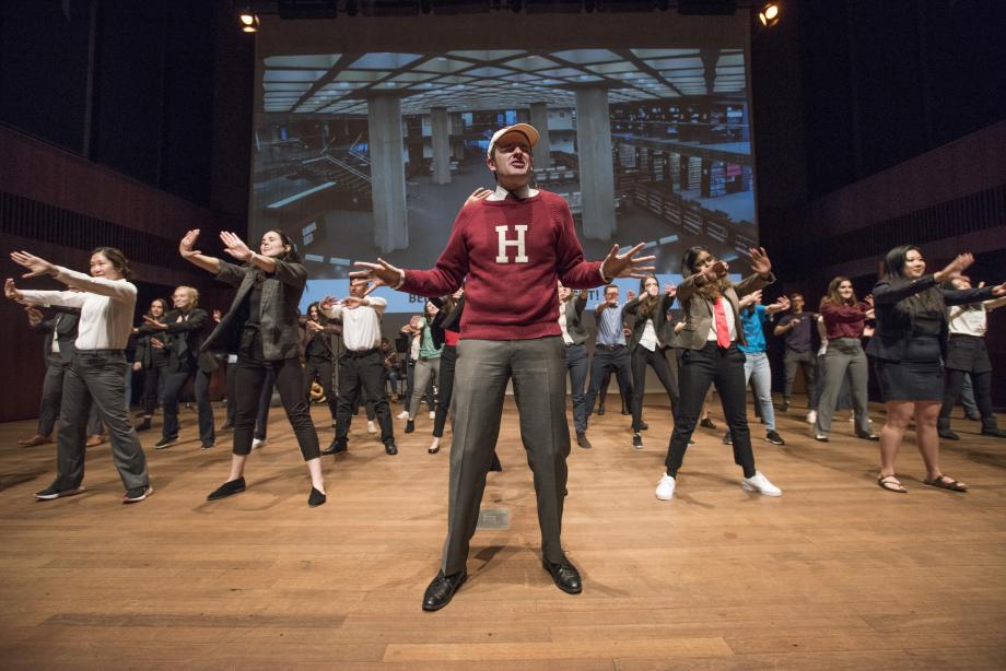 Eric Pawsner, wearing a red H sweater, sings as the rest of the cast looks on.