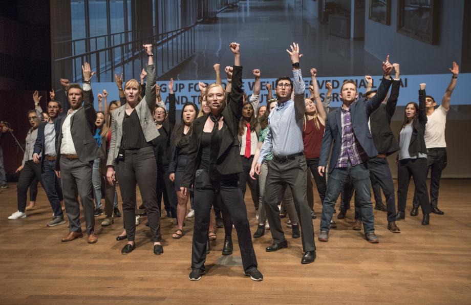 Student cast members on stage holding their fists in the air during one number.