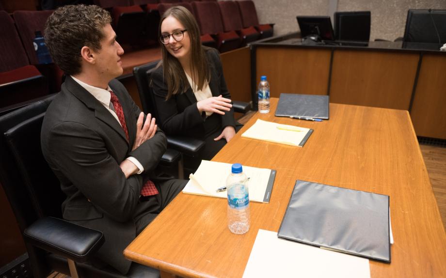 Two students talk while sitting at a table in the courtroom.