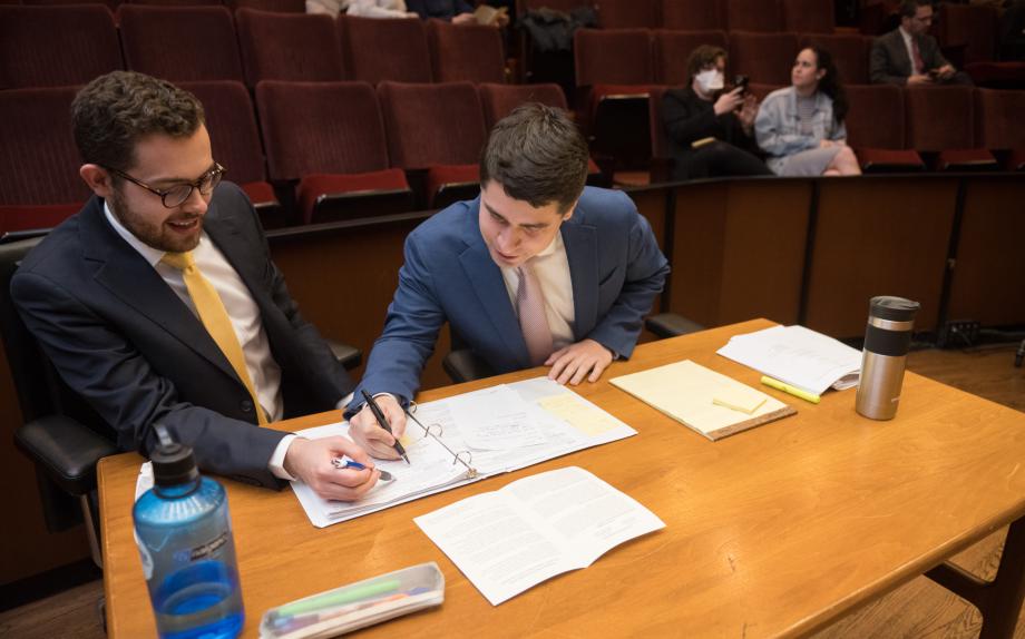 The other two students look at papers in front of them at their table.