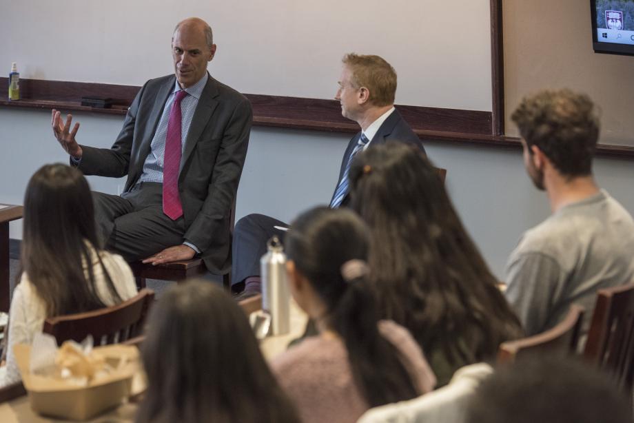 Justice Boasberg, sitting, gesticulates as Professor Masur looks on, students appear in the foreground, slightly out of focus