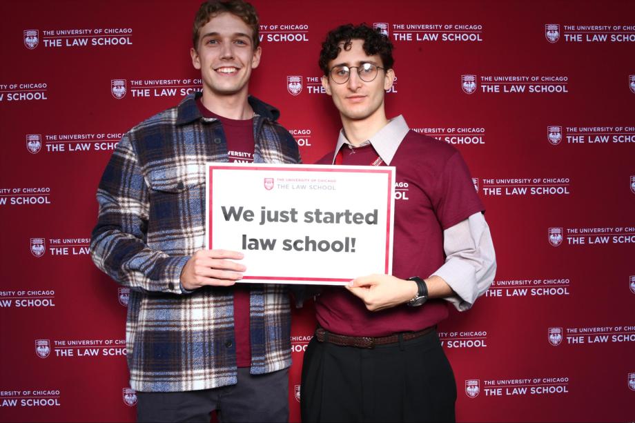Two people pose in front of a branded backdrop holding a sign, "we just started law school!"