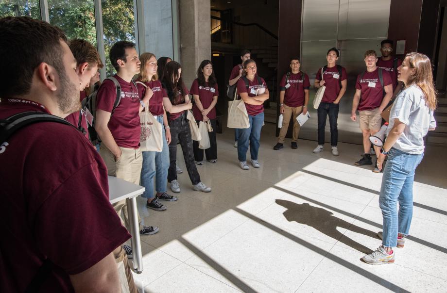Students form a semi-circle around an orientation leader in a hallway.