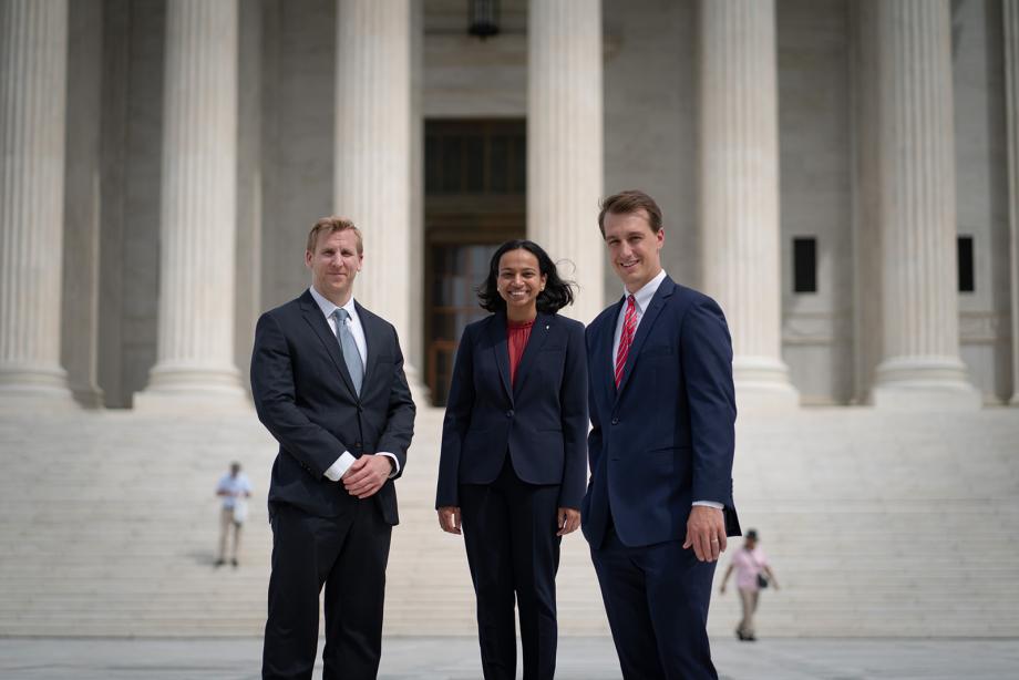 Three people in professional attire stand in fron the Supreme Court building