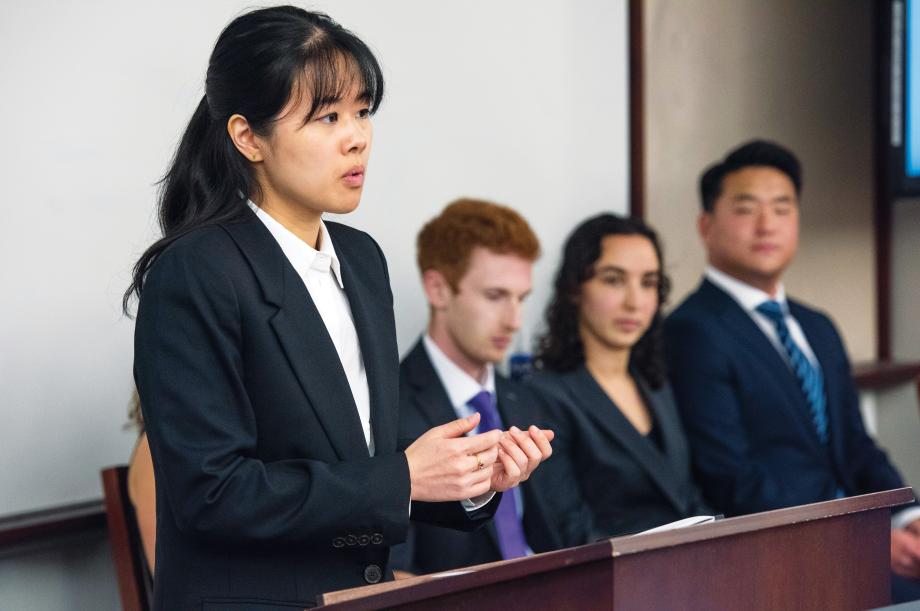 A person standing at a podium with 3 people sitting close to her