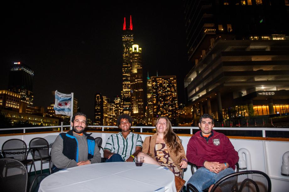 Four seated students pose for a photo on a boat on the Chicago River with city lights in the background.
