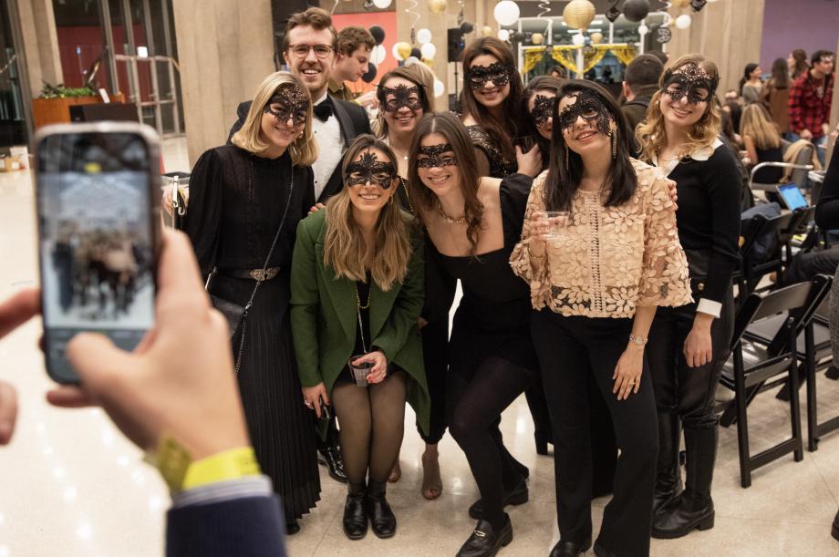 Someone holding a cell phone to take a photo of a group of nine students with masquerade masks.