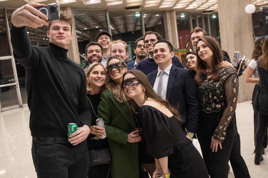 A group of 13 students pose for a selfie. Some wear masquerade masks and all are dressed up.