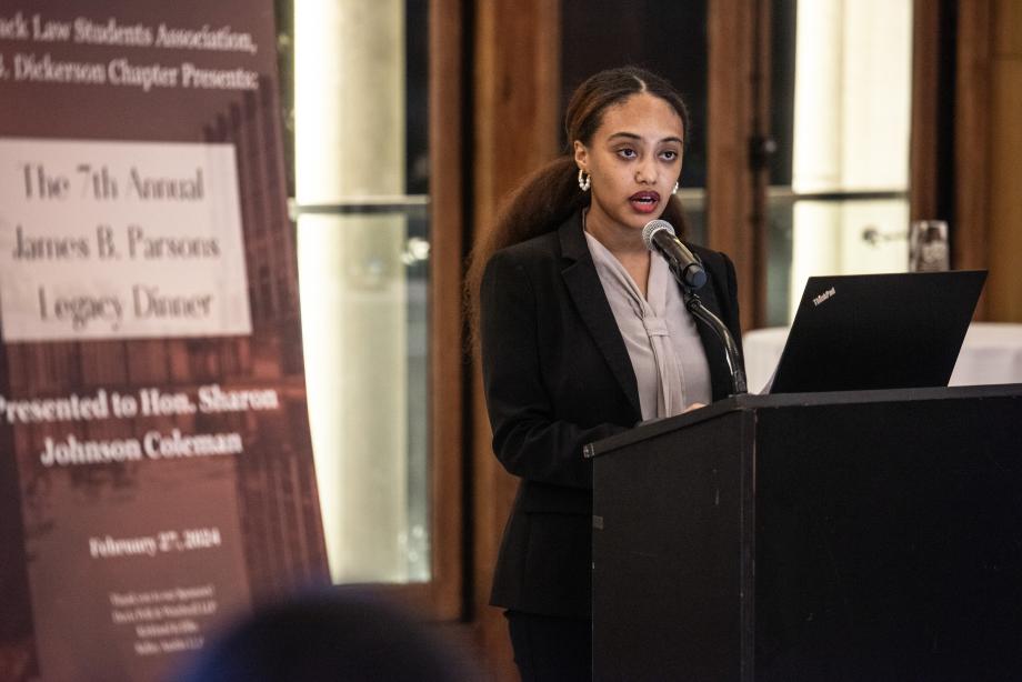 Hana Abreha wears a dark blazer over a blouse as she speaks from the podium.