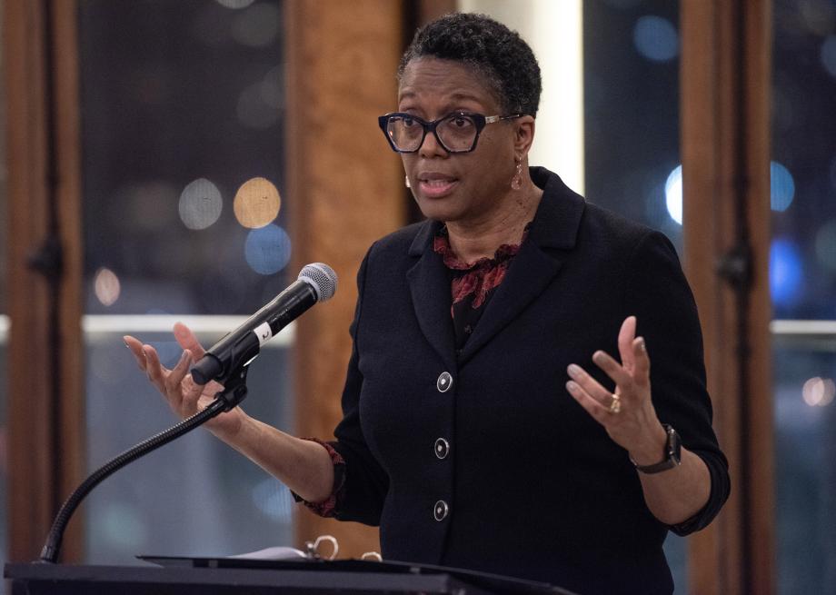 Sharon Johnson Coleman gesticulates with her hands as she speaks from the podium. She wears large-rimmed glasses and a black blazer over her blosue.